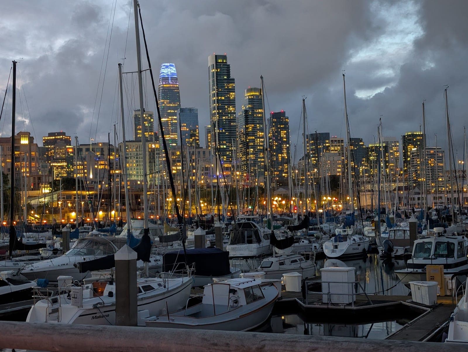 The San Francisco skyline glowing at night over a marina full of boats.