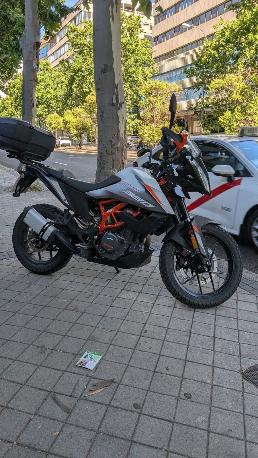 A white and orange adventure motorbike parked on a tiled pavement.
