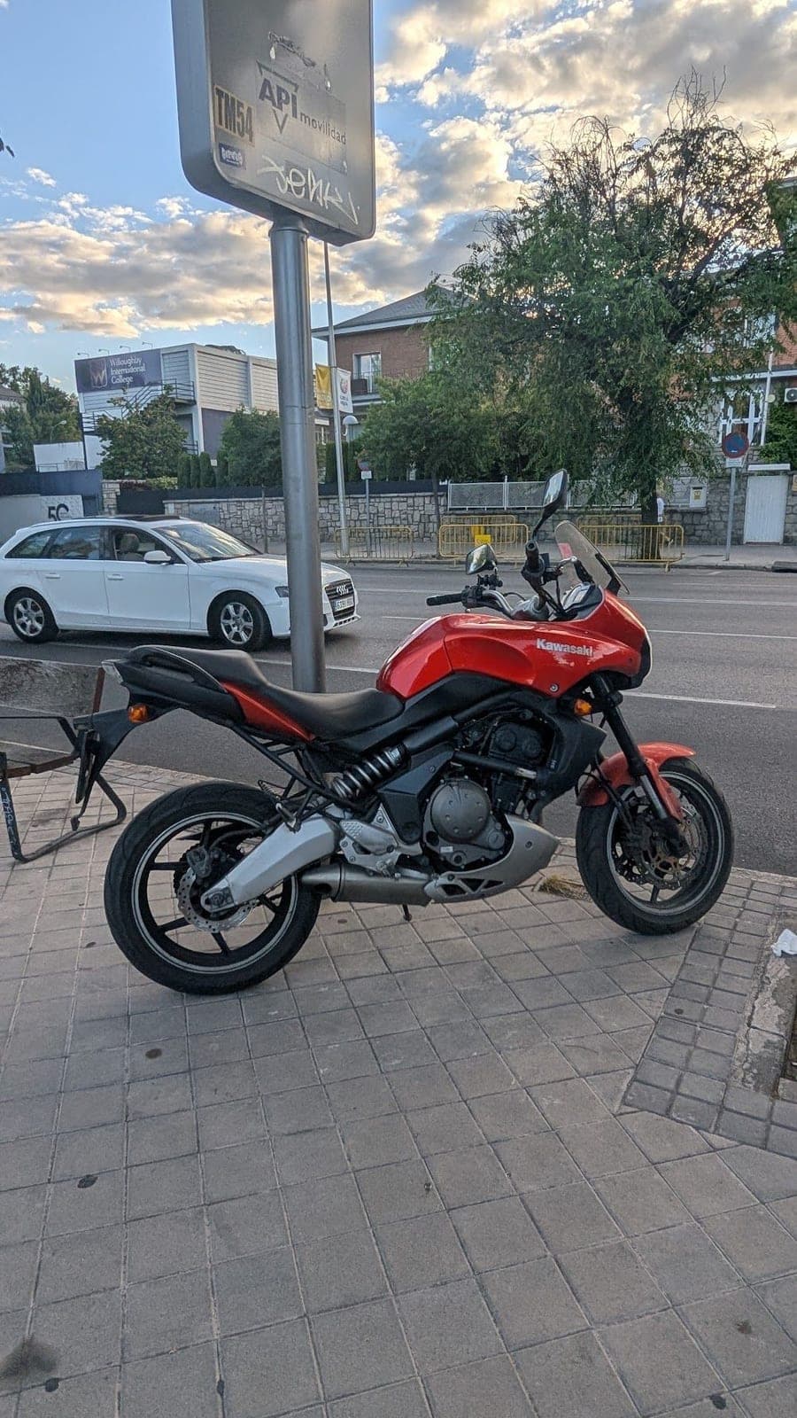 A red motorbike parked by a street sign at sunset.
