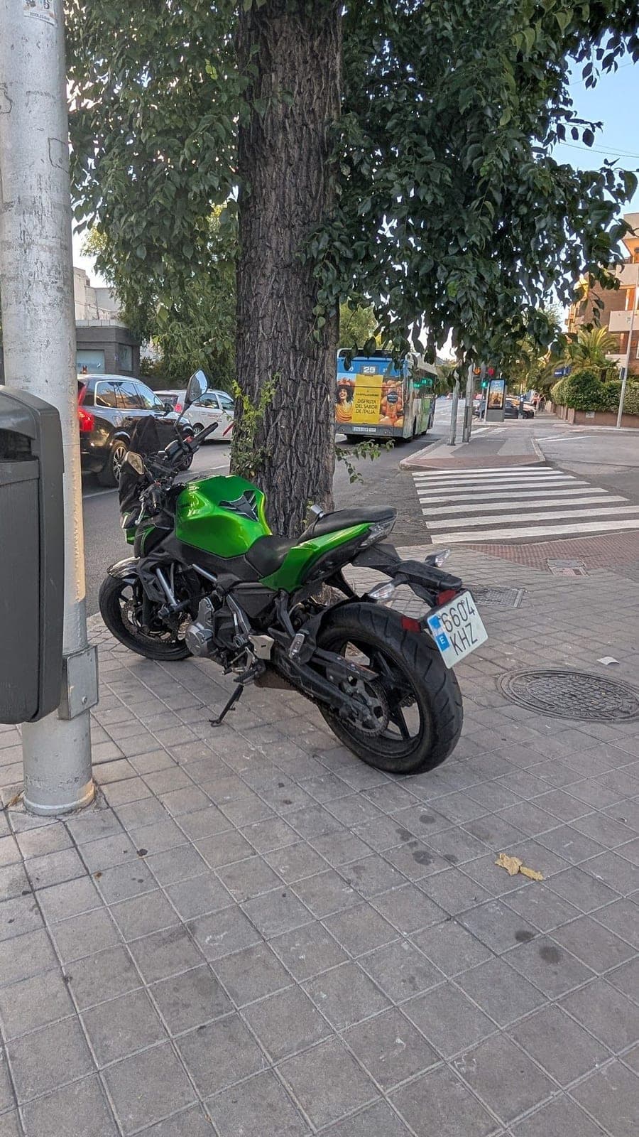 A green motorbike parked under a tree on a city street.
