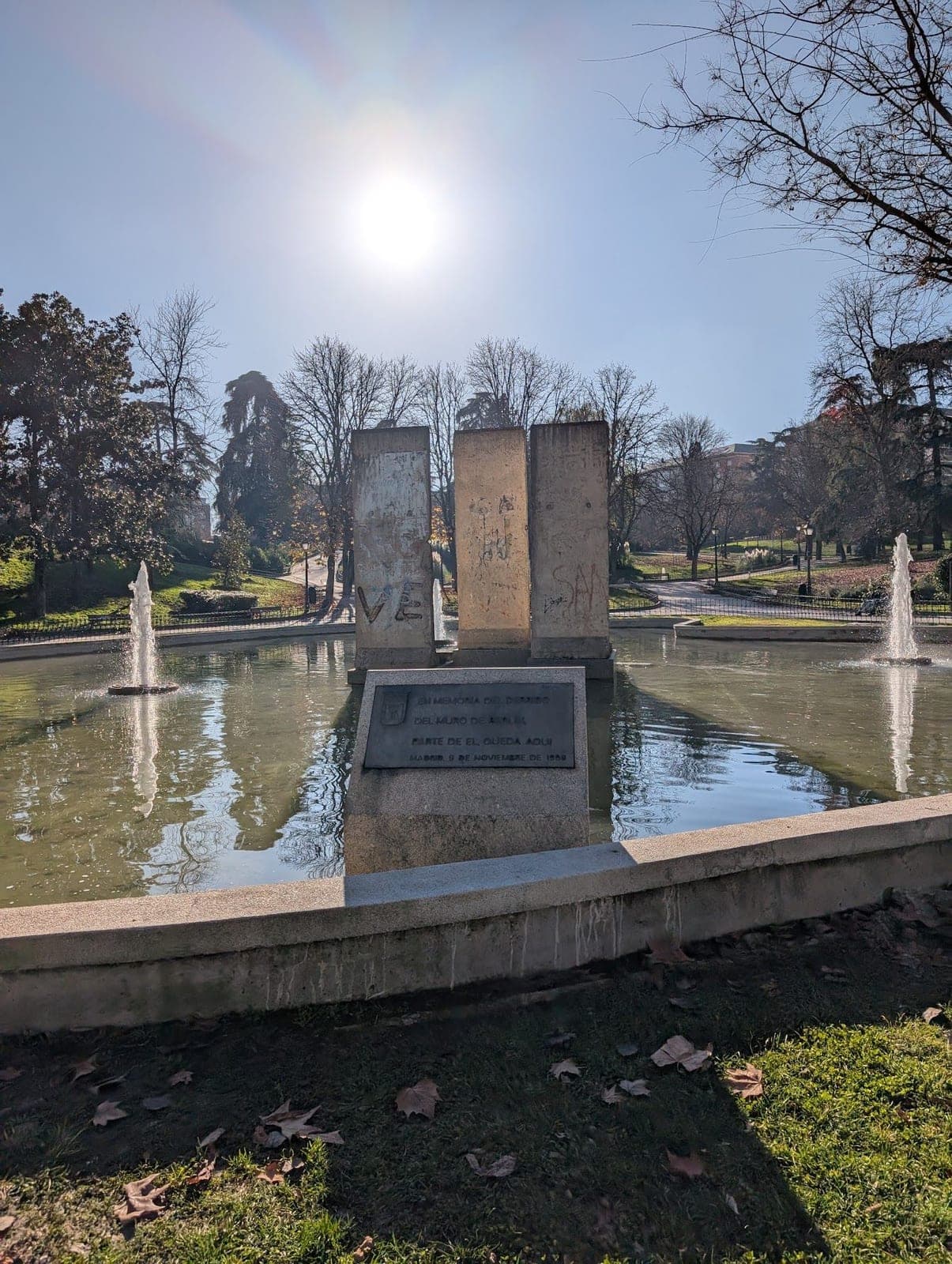 Three concrete slabs of the Berlin Wall standing in a fountain pond under a bright winter sun.