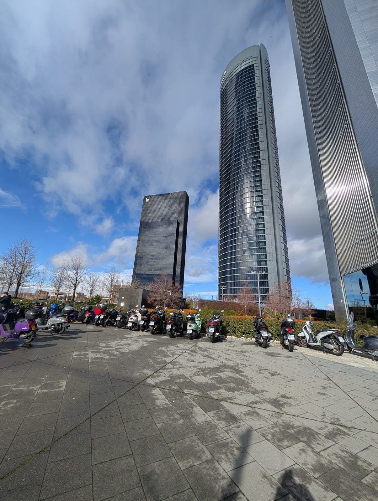 Glass skyscrapers of Madrid's Cuatro Torres against a blue sky, with motorbikes parked below.