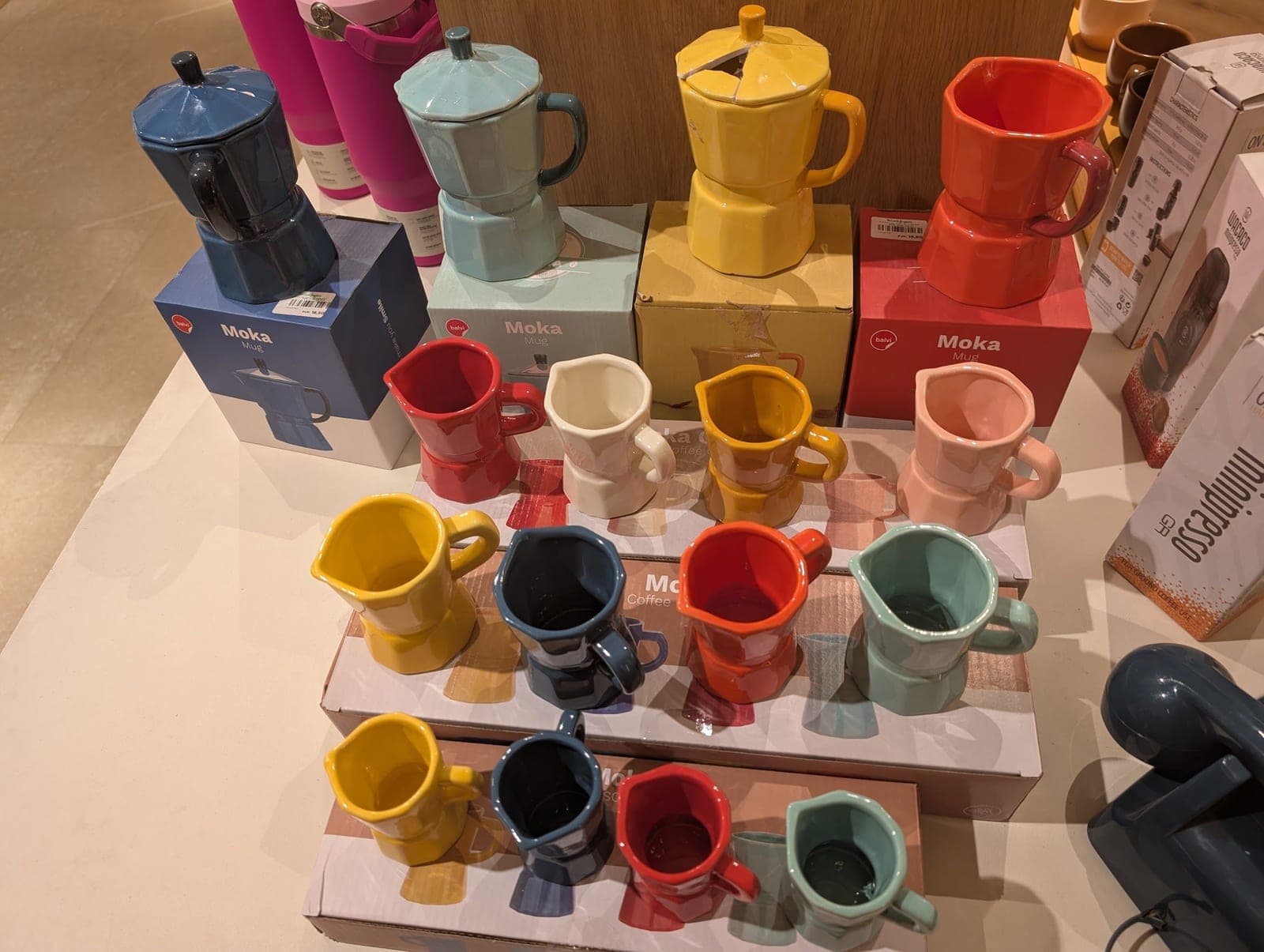 Moka pots and espresso cups in blue, yellow, red, pink and green on a shop display.