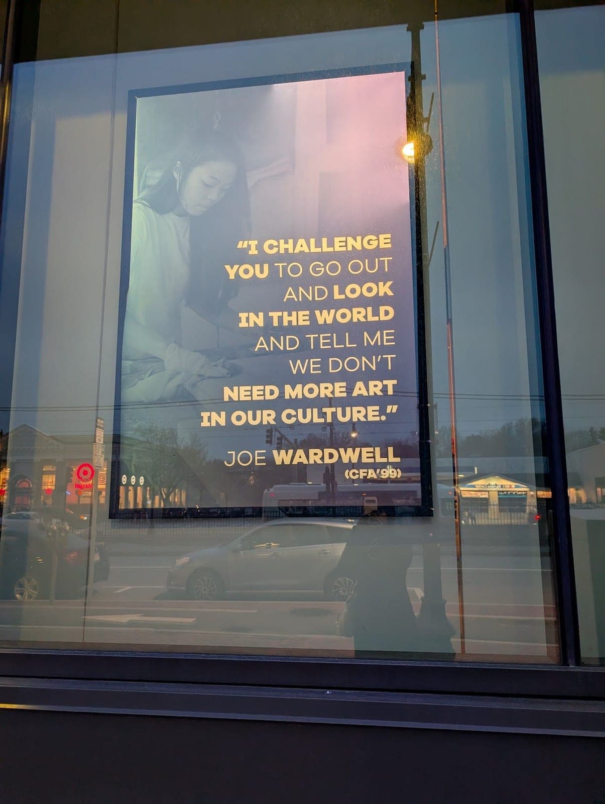 A poster in a window quoting Joe Wardwell: "I challenge you to go out and look in the world and tell me we don't need more art in our culture."