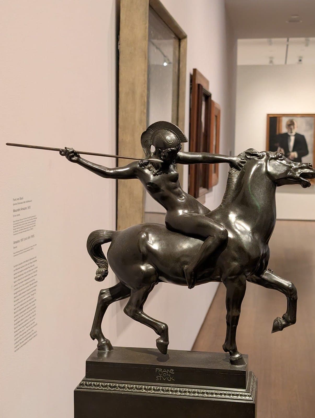 A small bronze of a woman in a crested helmet on a prancing horse, throwing a spear, in a gallery.
