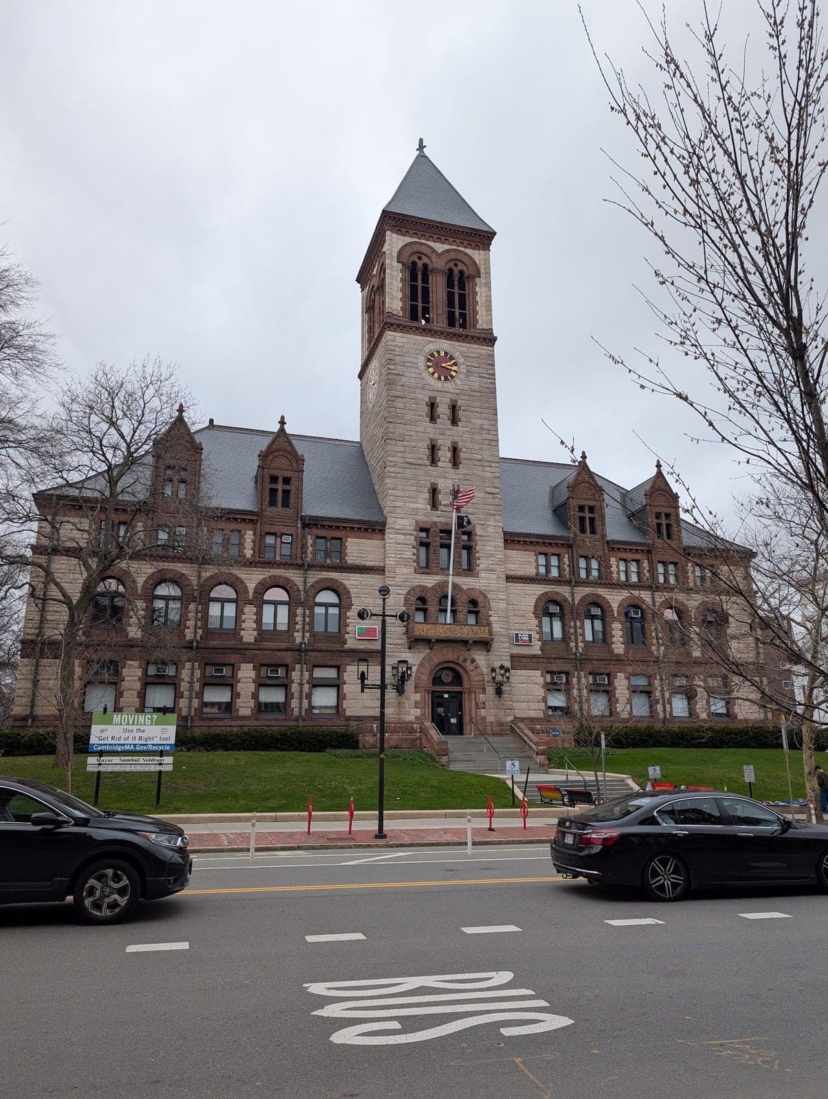 Cambridge City Hall, a stone building with a tall clock tower, cars passing in front.
