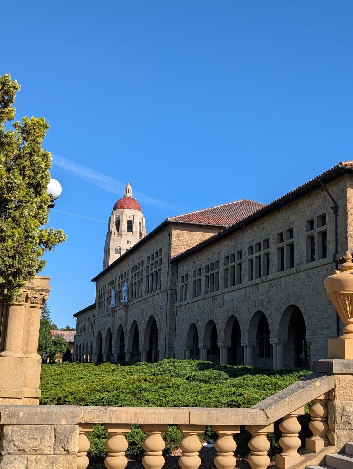 Sandstone arcades of the Stanford Main Quad and Hoover Tower under a deep blue sky.