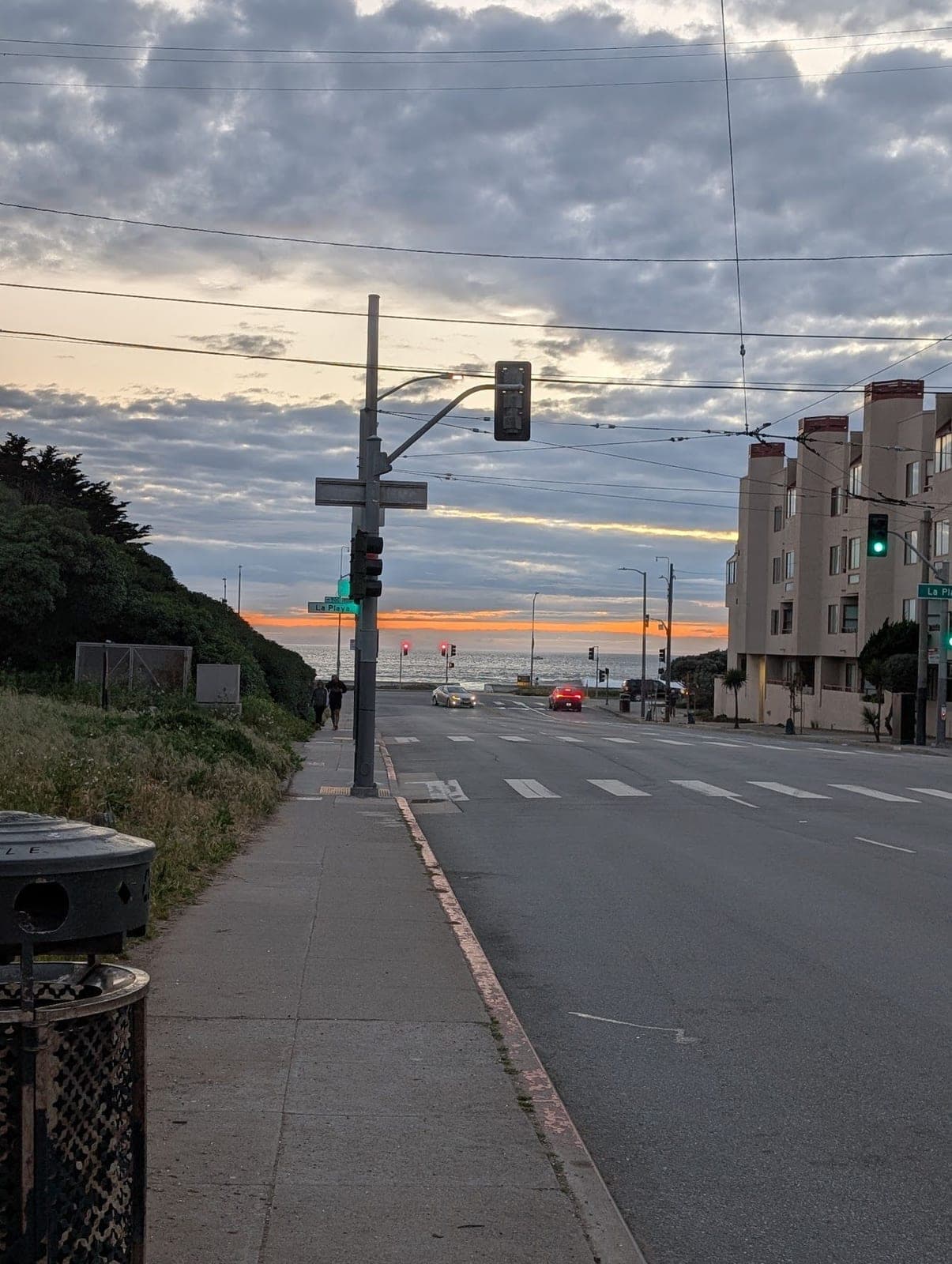 A wide street at sunset running down to the ocean, the sky orange at the horizon.
