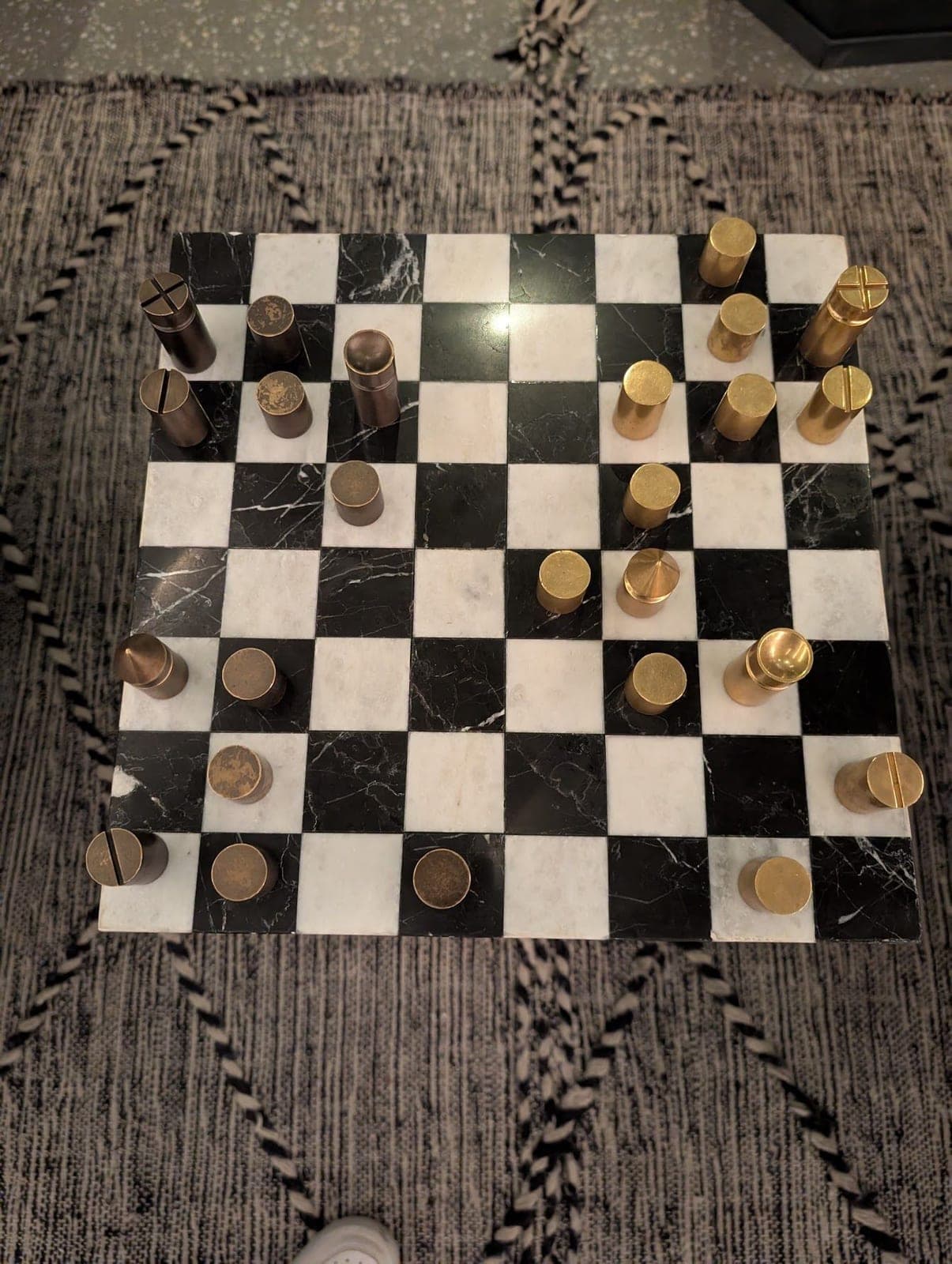 A marble chessboard seen from above, with gold and dark cylindrical pieces mid-game.