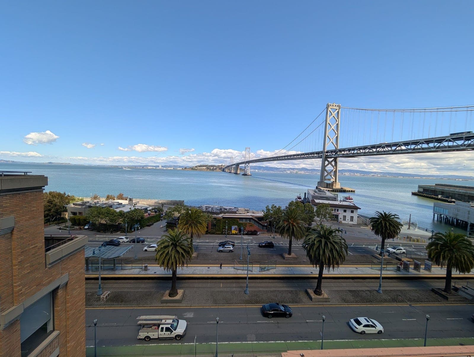 The Bay Bridge stretching over blue water, seen from above the palm-lined Embarcadero.