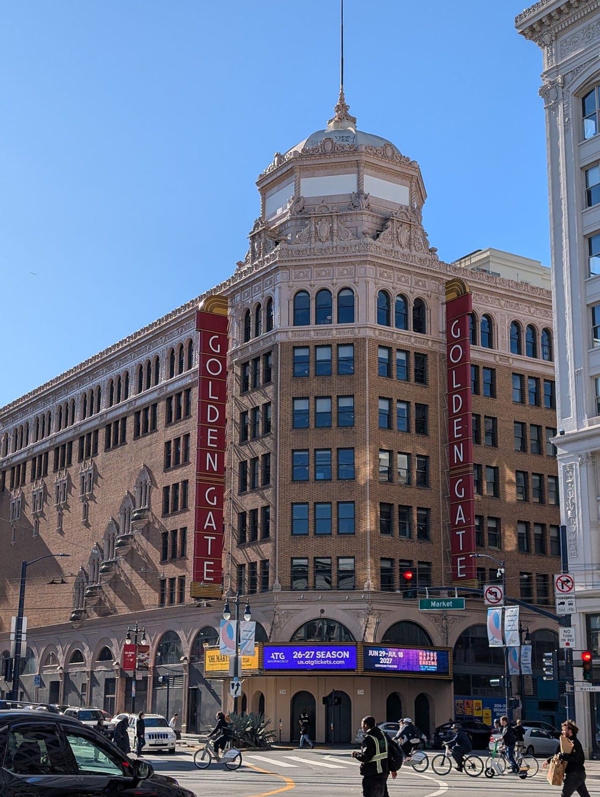 The domed brick Golden Gate Theatre on a street corner under a clear blue sky.