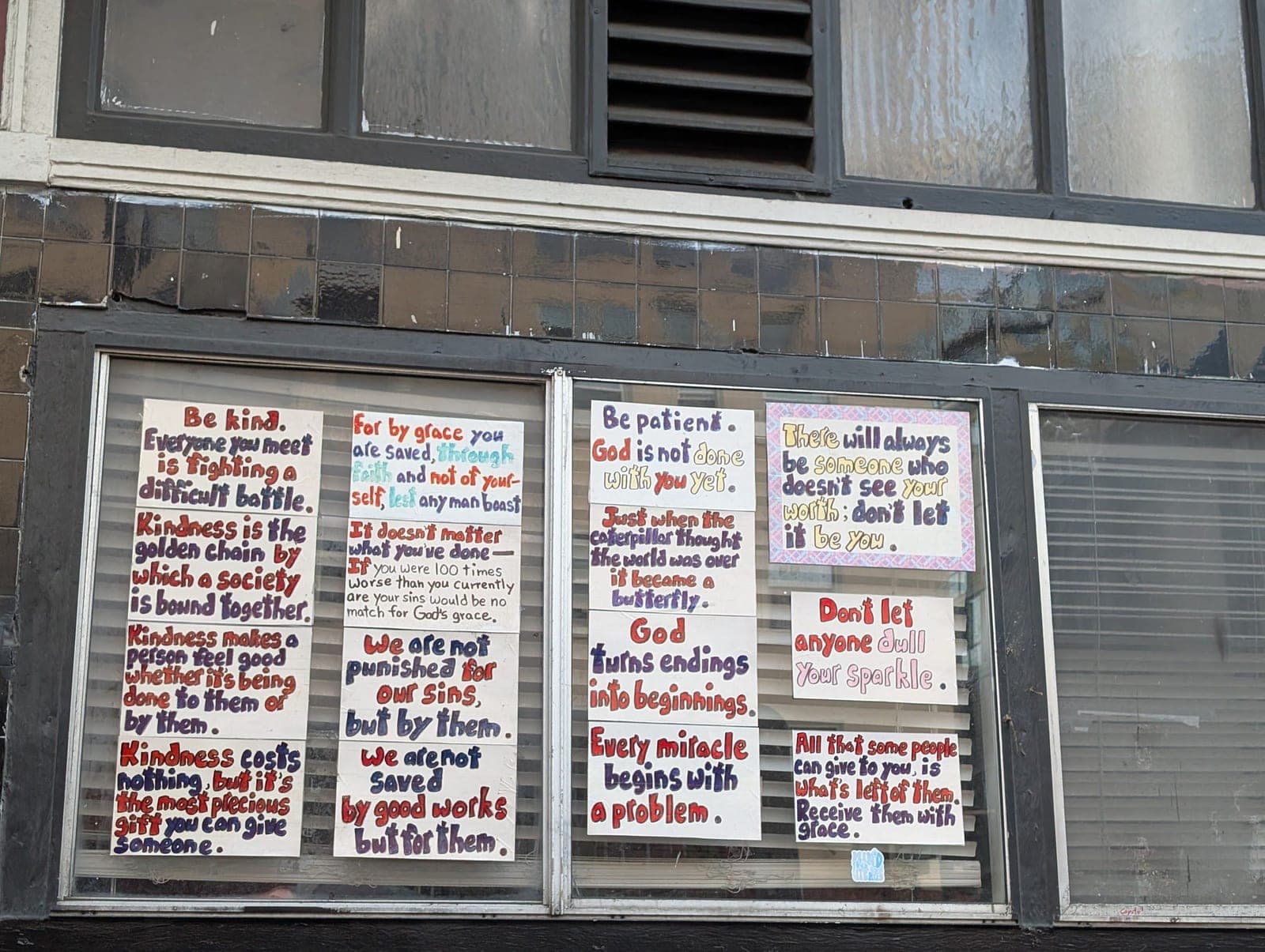 Hand-painted signs in a shop window with kind sayings, like "Be kind" and "Don't let anyone dull your sparkle".