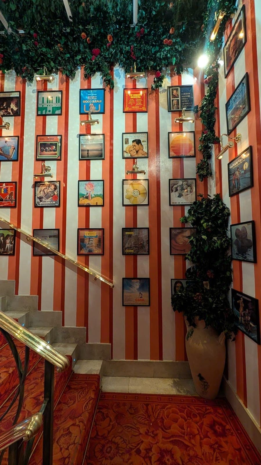 A staircase with red and white striped walls covered in framed record sleeves, plants hanging above.