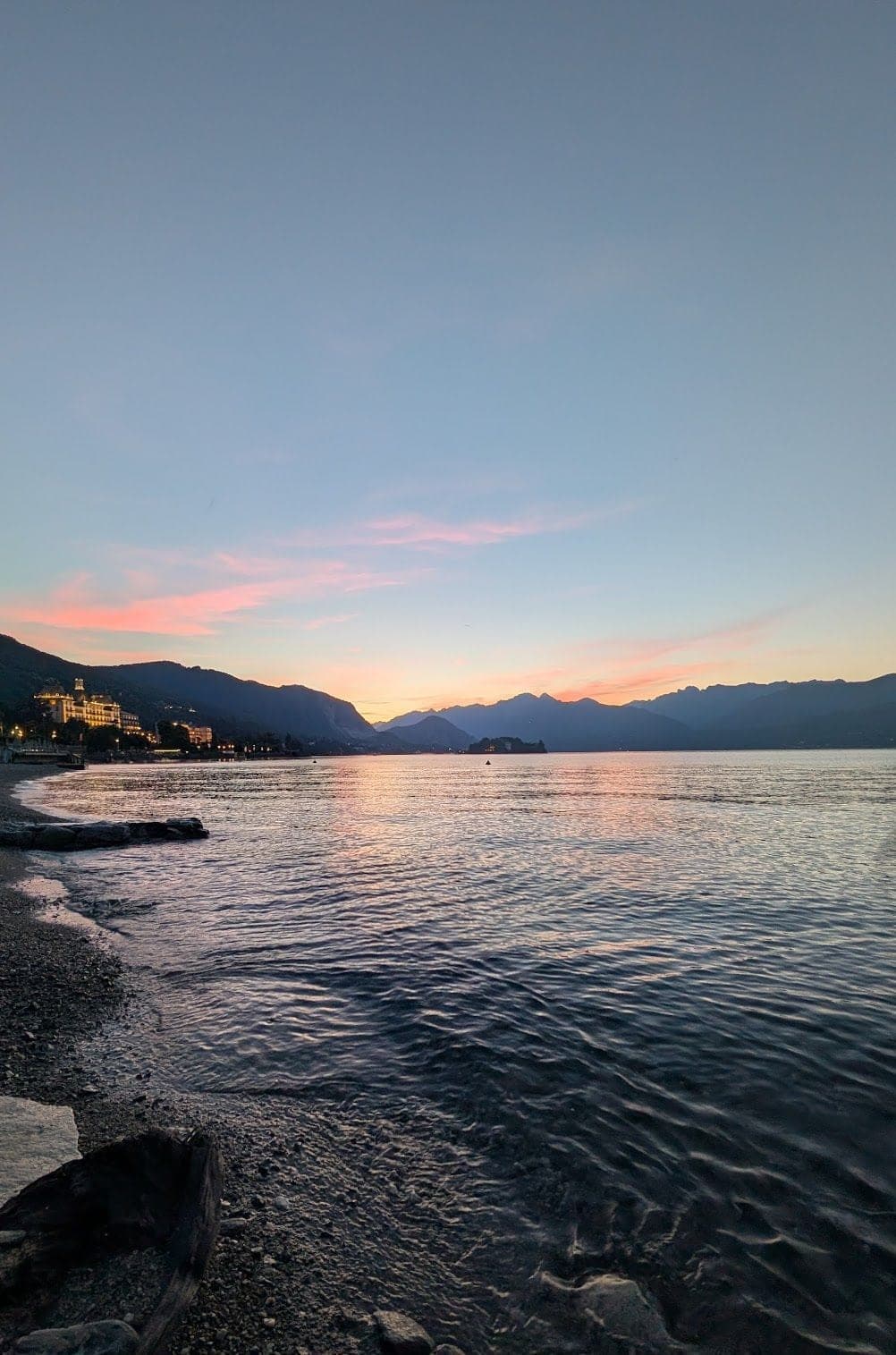 A calm lake at sunset, with mountains behind and a lakeside town lit up on the far shore.