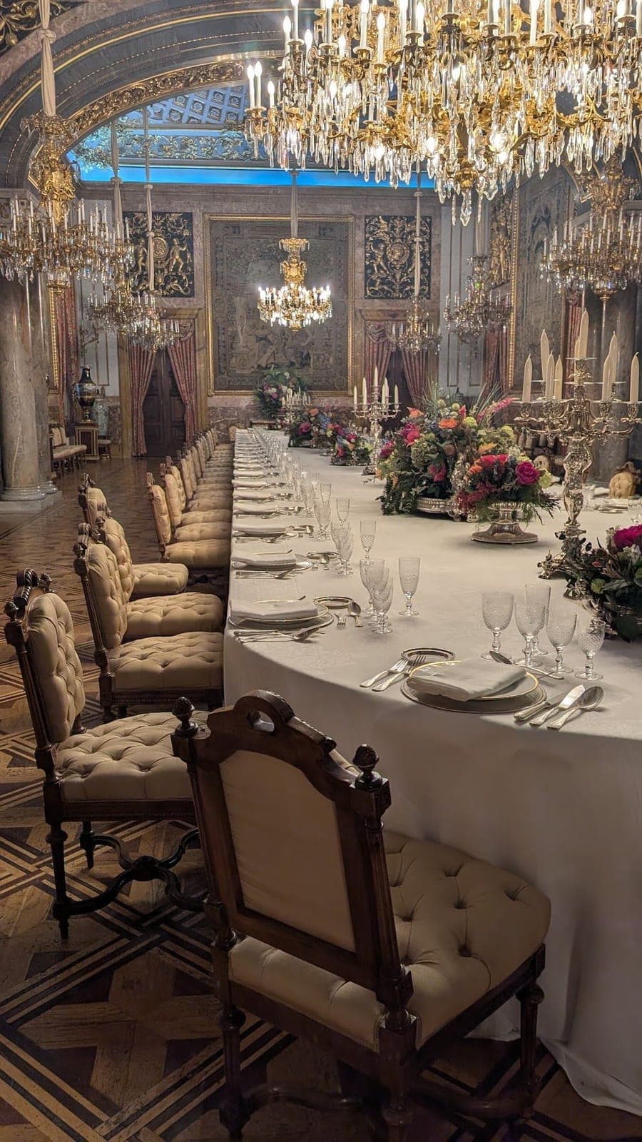A long banquet table set with glasses and flowers under crystal chandeliers.