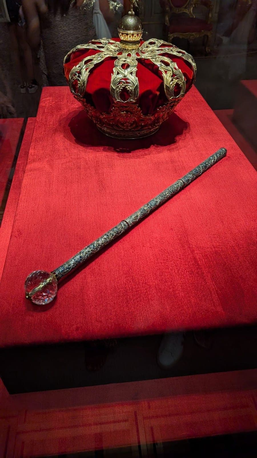 A red and gold crown and a jewelled sceptre on red velvet.