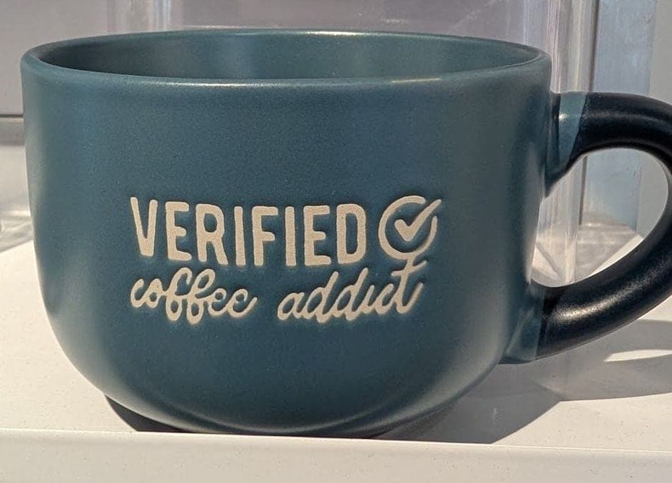 A blue mug on a shop shelf that says "Verified coffee addict".