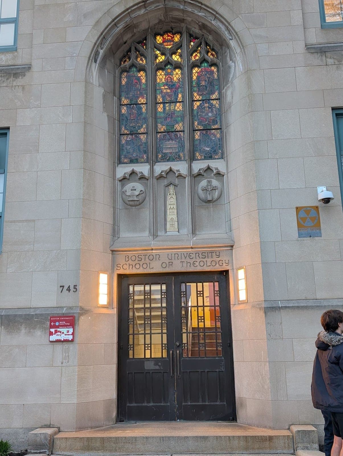 The stone entrance of the Boston University School of Theology, with a tall stained-glass window above its doors.
